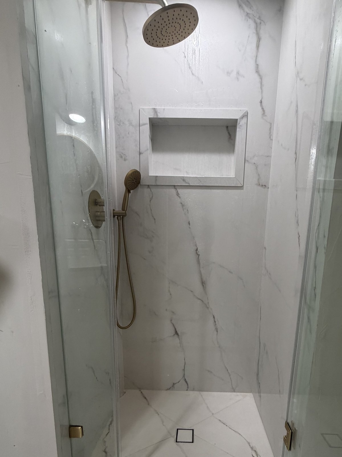 The same alcove in Calacatta Oro porcelain with frameless glass and a recessed niche.