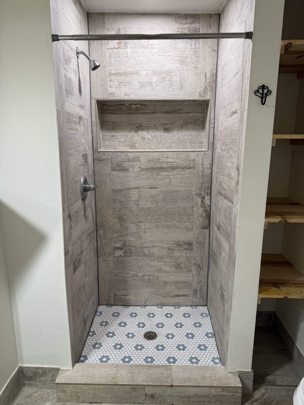 Shower alcove finished in wood-look plank tile with a hex mosaic floor.