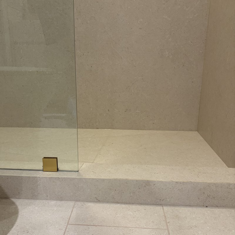 Shower curb and pan meeting the bathroom floor in matching porcelain.