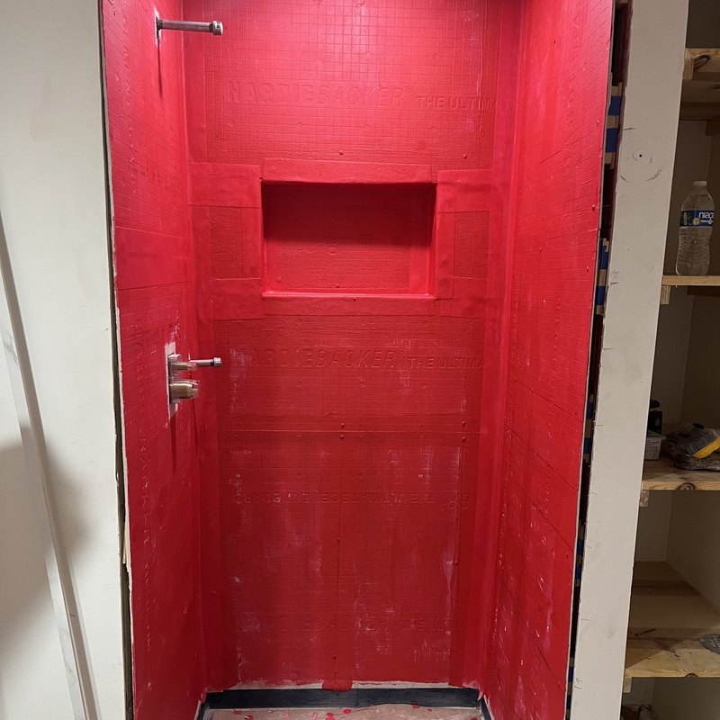 Shower walls in cement backer board coated with red waterproofing membrane.