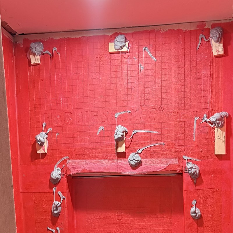 Construction adhesive applied in dabs across the waterproofed wall, with wood shims.