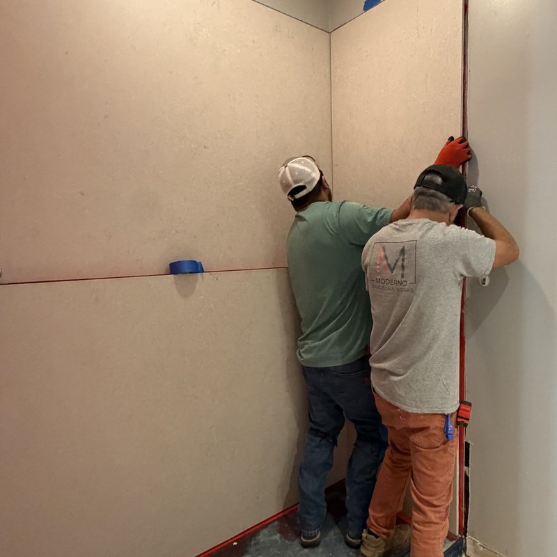 Two installers lifting a full-height porcelain panel into a corner.